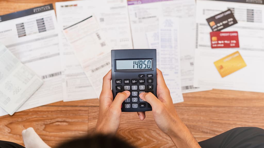 Mostrar uma pessoa com uma calculadora na mão fazendo contas sobre suas dívidas