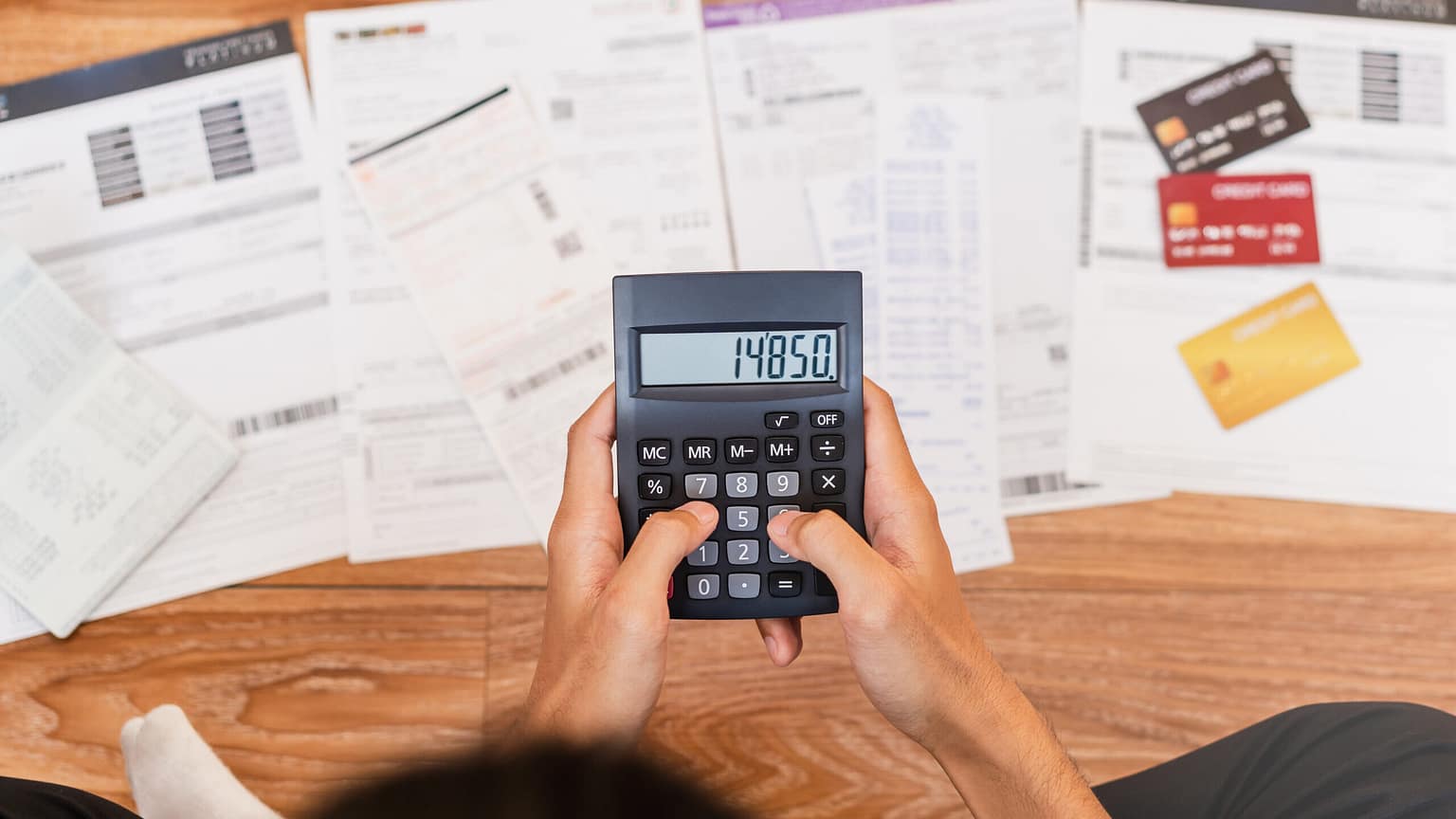 Mostrar uma pessoa com uma calculadora na mão fazendo contas sobre suas dívidas